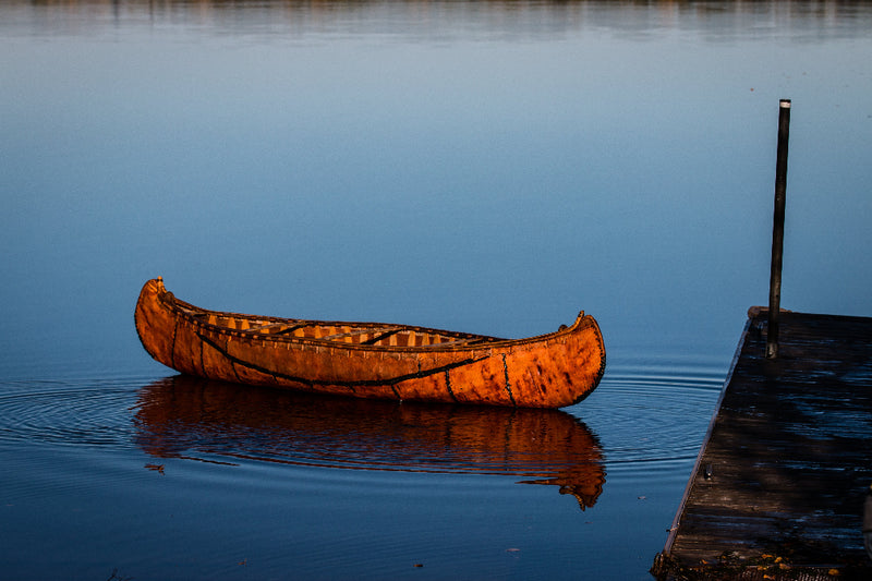 Wooden canoe on a calm body of water near a dock at sunset.