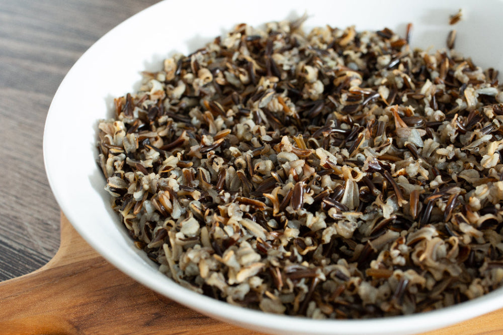 Cooked wild rice in a white bowl on a wooden surface